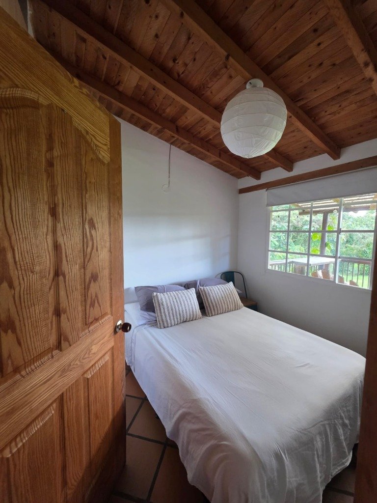 Habitación principal amoblada con cama vestida, techo rústico de madera y ventana campestre en Casa Campestre La Isabela La Ceja